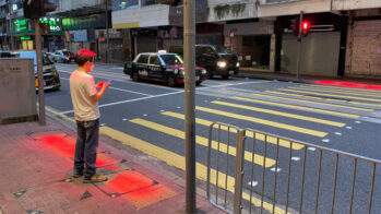 Peão com telemóvel à espera de passar na passadeira em Hong Kong