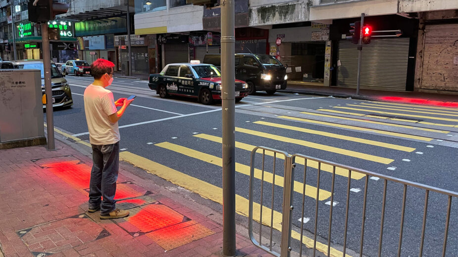 Peão com telemóvel à espera de passar na passadeira em Hong Kong