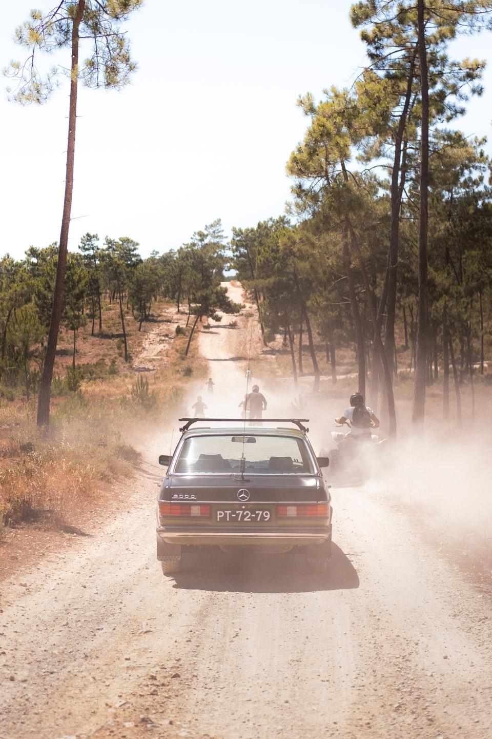 Mercedes W123 em caminho de gravilha, a ser ultrapassado por quads e motas