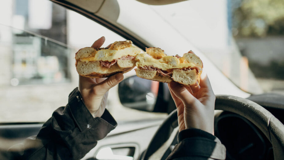 Pessoa a comer uma sandes ao volante