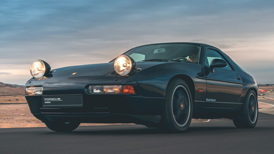 Porsche 928 com faróis escamoteáveis ligados, frente 3/4 em pista