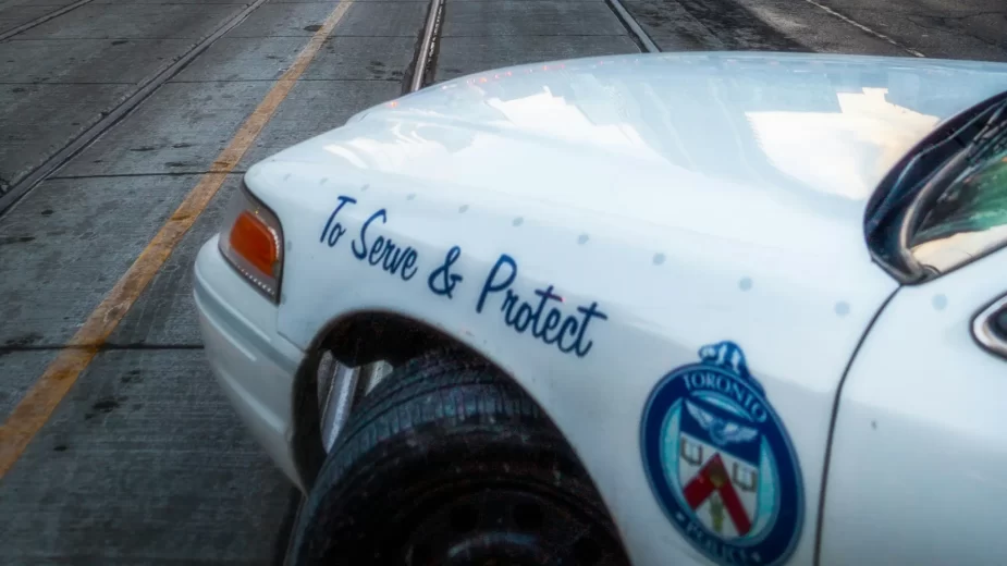 Detalhe de carro de polícia com inscrição "To Serve and Protect"